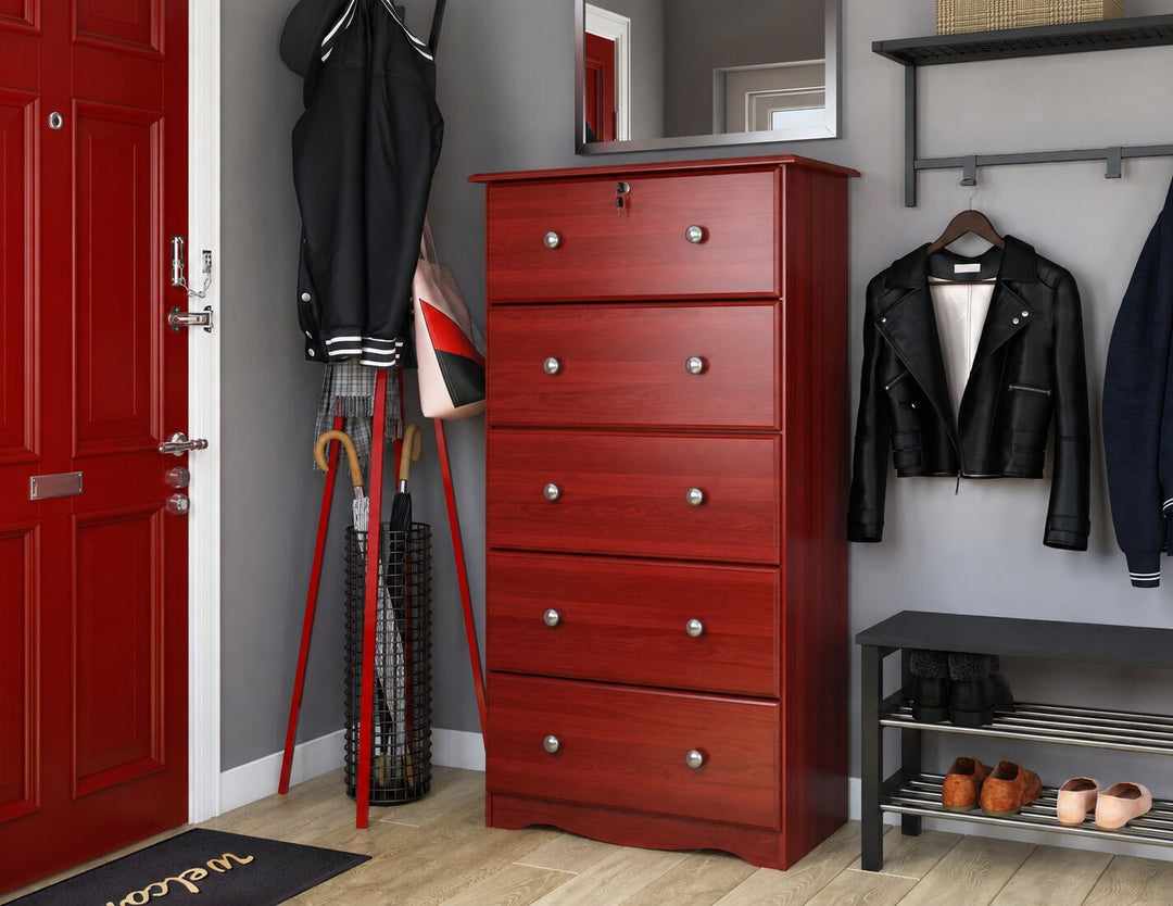 A five-drawer chest of drawers in a reddish-brown Mahogany wood finish with silver knobs, positioned in a modern entryway next to a red door, with jackets and shoes displayed around it.